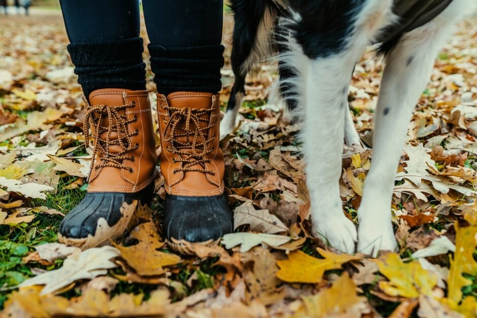 person in brown-and-black duck boots stands beside dog